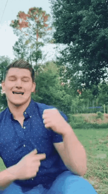 a young man in a blue shirt is sitting in a grassy field