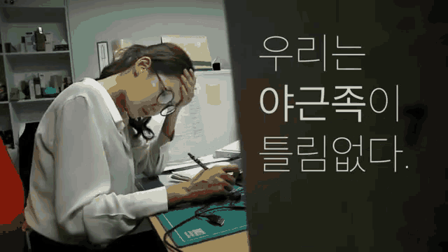 a woman sitting at a desk with her hand on her head and a sign that says ' 우리 는 '