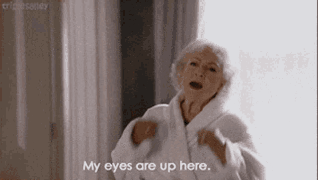 an elderly woman in a robe is standing in front of a window and says `` my eyes are up here '' .