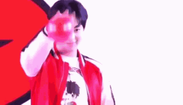a young man in a red jacket is holding a red balloon in front of his face .
