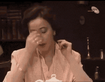a woman is sitting at a table with a cup of tea in her hand and covering her face with her hand .
