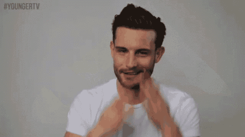 a man with a beard is wearing a white t-shirt and waving his arms in the air .
