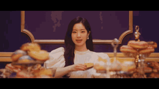 a woman in a white dress is sitting in front of a table full of desserts