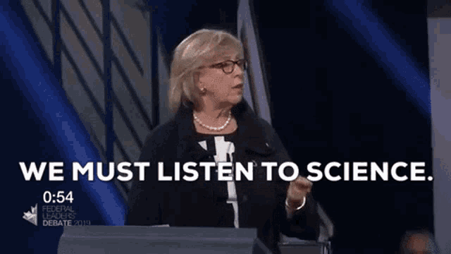 a woman speaking on a stage with the words we must listen to science behind her