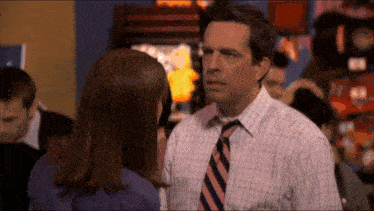 a man in a plaid shirt and tie stands next to a woman in a blue shirt