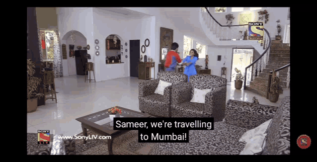 a television screen shows a man and woman standing in a living room with the words " sameer we 're travelling to mumbai "