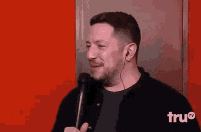 a man with a beard is holding a microphone and wearing ear buds .