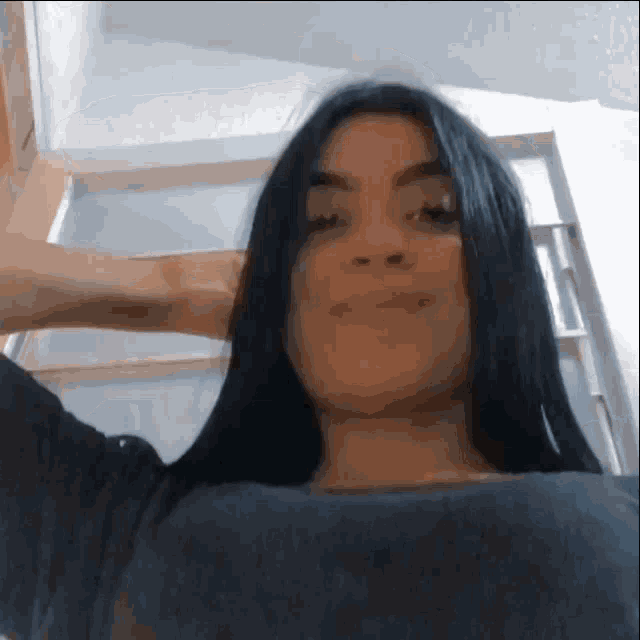 a woman with long black hair is standing in front of a door with her hand on her head .