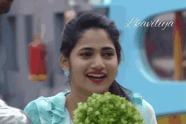a woman is smiling and holding a bunch of lettuce in front of a sign that says lkavicya