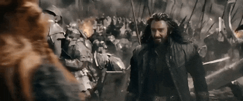 a man with a beard is standing in front of a crowd of soldiers in armor .