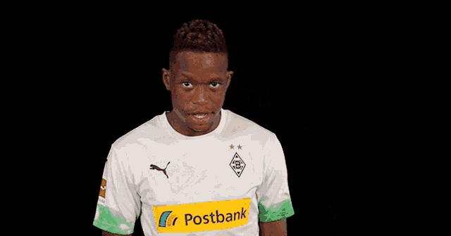 a man wearing a postbank jersey wipes his forehead with his hand