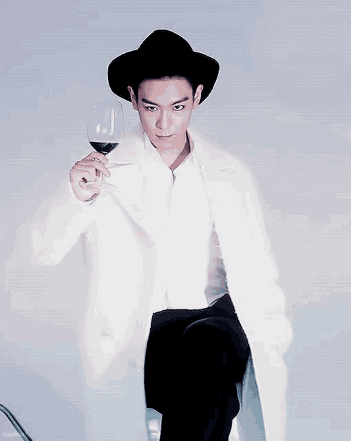 a man wearing a black hat and a white coat holds a glass of wine