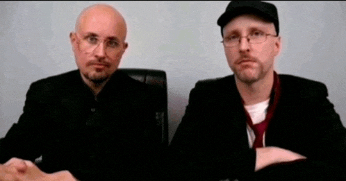 two men sitting next to each other wearing glasses and ties