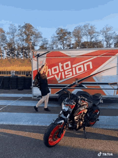 a woman stands next to a motorcycle in front of a photo vision truck