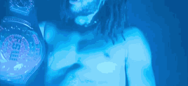 a shirtless man with dreadlocks is holding a wrestling belt in a dark room .