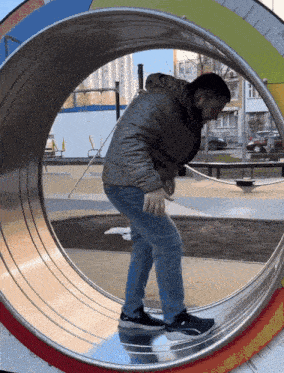 a man is walking through a metal tube in a park while wearing a gray jacket