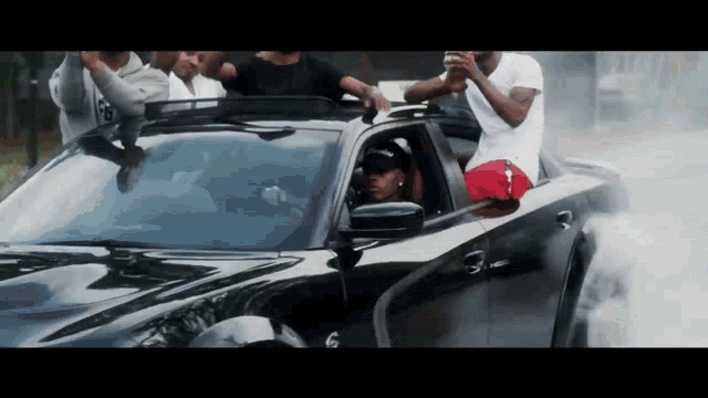 a group of men are standing on top of a black car with a roof rack