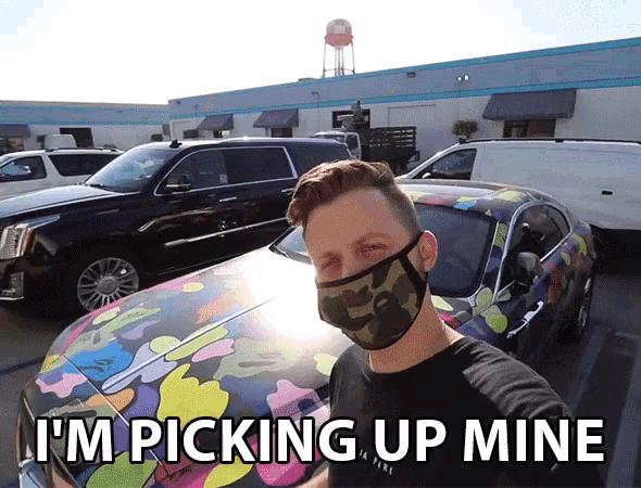 a man wearing a face mask is standing in front of a car that says i 'm picking up mine