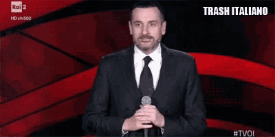 a man in a suit and tie is holding a microphone in front of a red background that says trash italiano on it