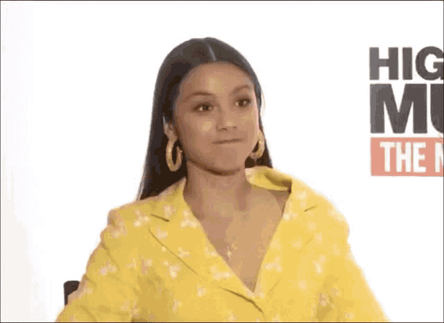 a woman in a yellow jacket is laughing in front of a sign that says hig mu the n