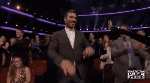 a man in a suit is dancing in front of a crowd of people at the american music awards