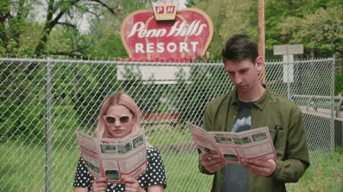 a man and a woman are reading a map in front of a penn hills resort sign .