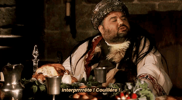a man in a costume is sitting at a table with food and says " interprrrrte ! couilere "