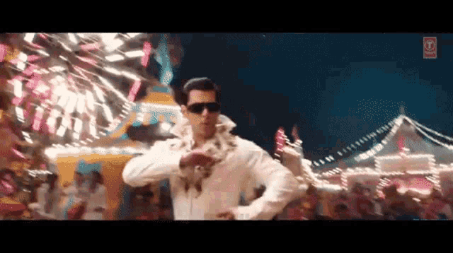 a man wearing sunglasses and a white shirt is dancing in front of a crowd of people .