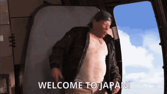 a man in a black jacket is standing in front of a sign that says " welcome to japan "