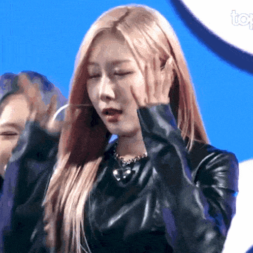 a woman wearing a black leather jacket covering her face with her hands
