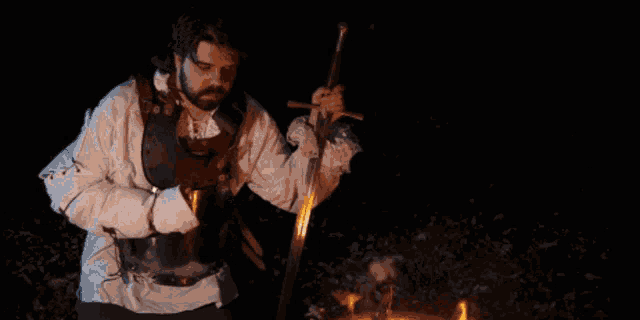 a man with a beard is holding a sword in front of a fire