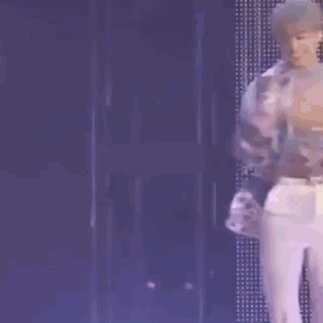 a man in white pants is dancing on a stage in front of a purple background .