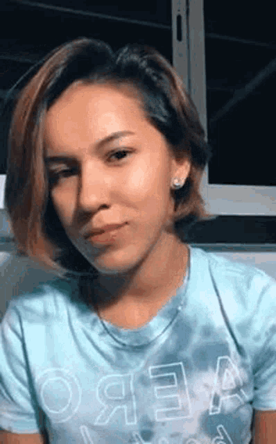 a young woman with short hair is wearing a blue tie dye t-shirt .