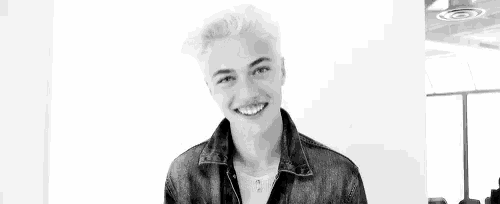 a black and white photo of a young man in a leather jacket making a funny face .