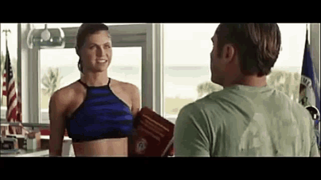 a man and a woman are standing next to each other in front of a window . the woman is holding a book .