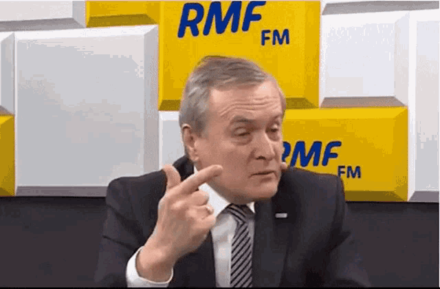 a man in a suit and tie is giving a thumbs up in front of a wall with rmf fm on it .