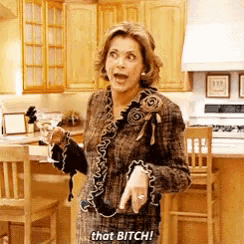 a woman is standing in a kitchen holding a purse and saying that bitch !
