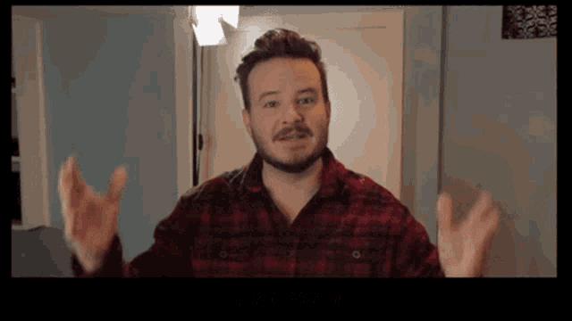 a man with a beard wearing a red plaid shirt is making a funny face