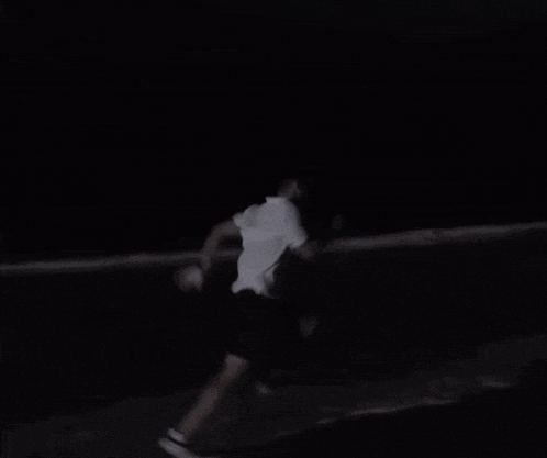 a man in a white shirt and black shorts is running in the dark