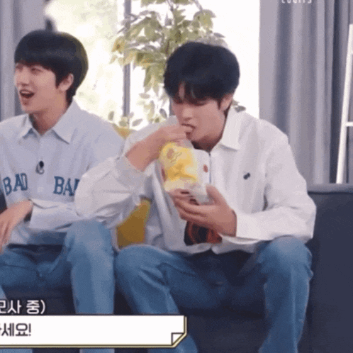two young men are sitting on a couch with one wearing a shirt that says bad bad