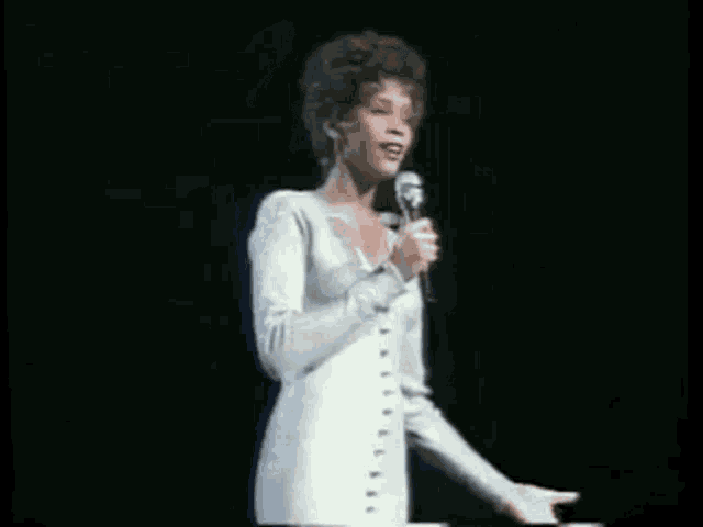 a woman in a white dress is holding a microphone on a stage .
