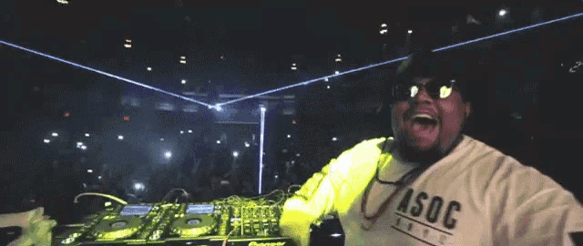 a man wearing sunglasses and a shirt that says asoc is standing in front of a crowd