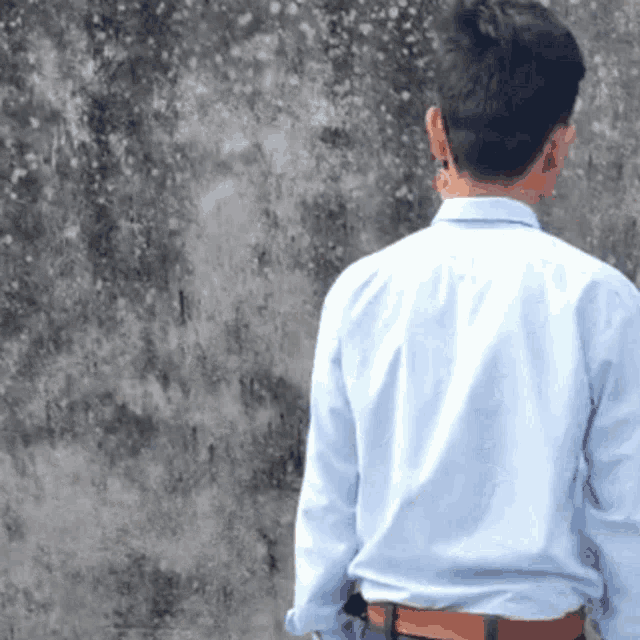 a man in a blue shirt is standing in front of a concrete wall .