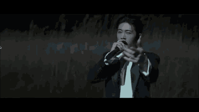 a man in a suit is singing into a microphone while standing in a field .