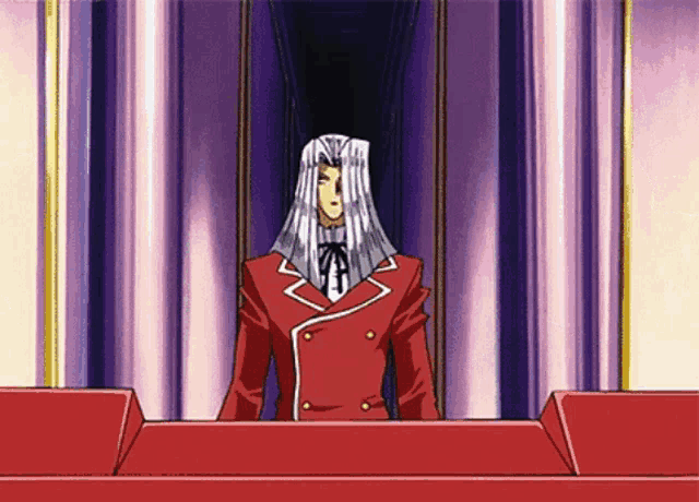 a man in a red suit and white tie stands in front of a pink curtain