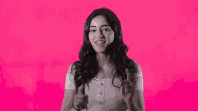 a woman is standing with her arms in the air and a pink background .