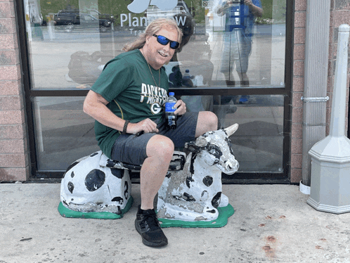 a man wearing a green shirt that says dairy north g is sitting on a cow statue