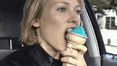 a woman in a car is eating an ice cream cone with blue ice cream