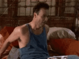 a man in a blue tank top is laying in bed .