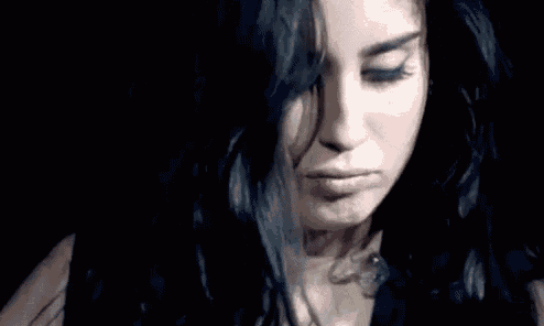 a close up of a woman 's face with black hair and blue eyes in a dark room .